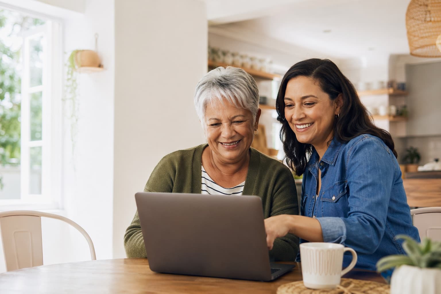 A senior woman and her adult daughter smiling while reviewing Medicare options on a laptop at home